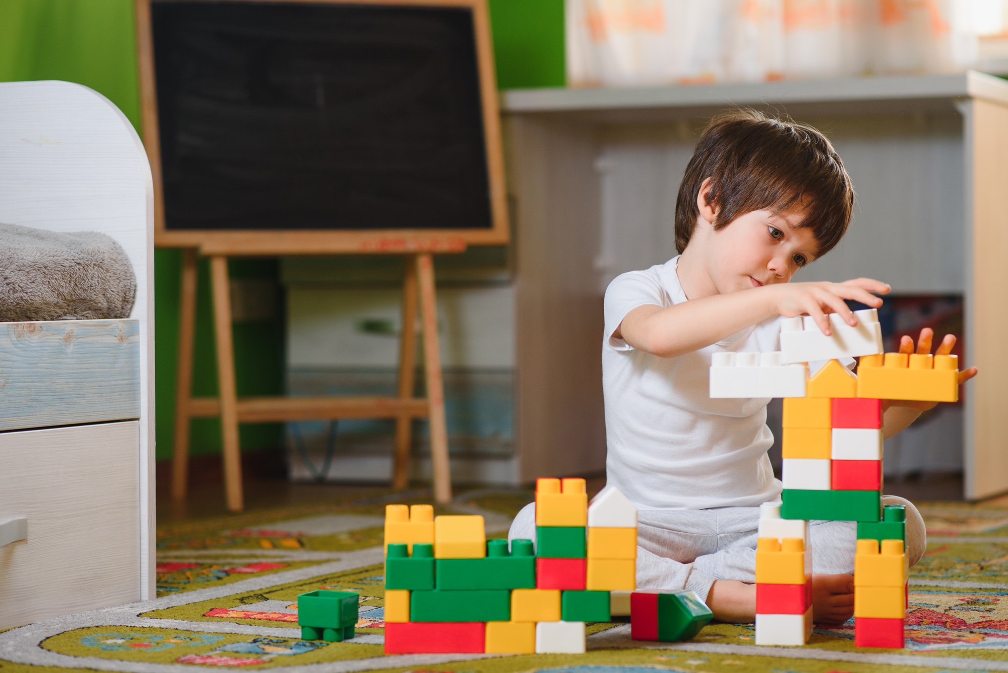 child little boy playing with wooden cubes toys in nursery at home or daycare center